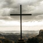 A powerful silhouette of a cross set against a dramatic cloudy mountain landscape.